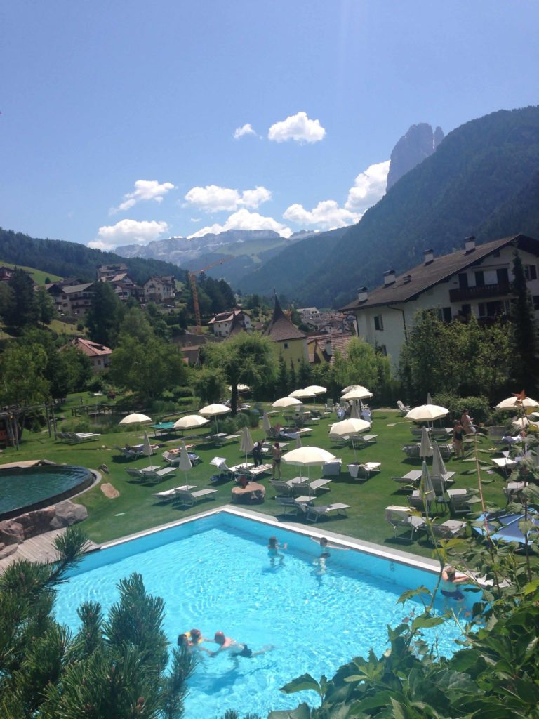 Blick auf Garten mit Liegewiese und Pool und Berge Adler Dolomiti Spa & Sport Resort