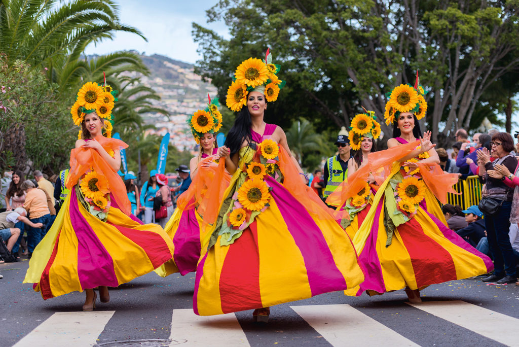 MIt Blumen geschmückte Frauen in Kleidern, die tanzend mit der Parade mit gehen 