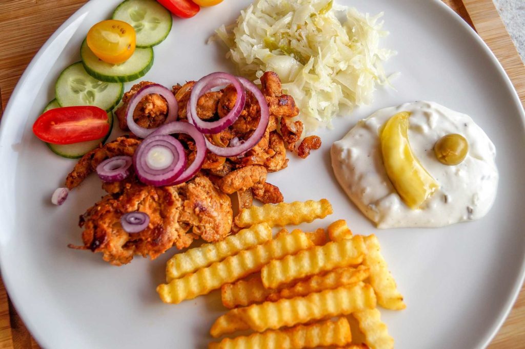 Gyros auf einem Teller mit Tsatziki, Pommes, Krautsalat und Gurken