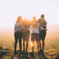 Vier Menschen die sich in den Armen halten und auf den Sonnenuntergang gucken