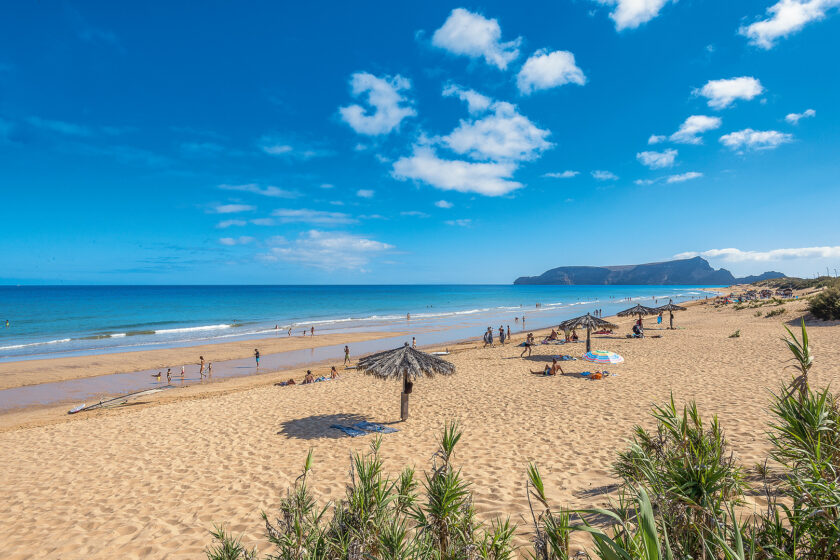 Sandstrand mit blauem Meer auf Madeira. Im Hintergrund Berge