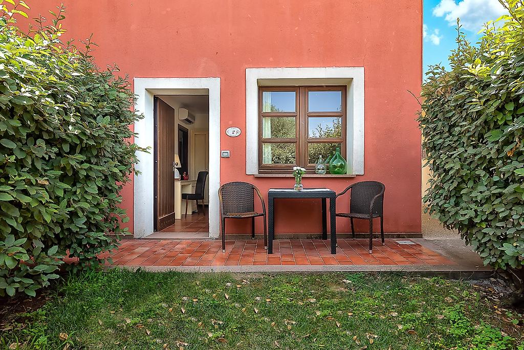 Alghero Resort Country Hotel, Privater Patio eines Zimmers mit Sitzgelegenheit, umgeben von typisch italienischem Flair.