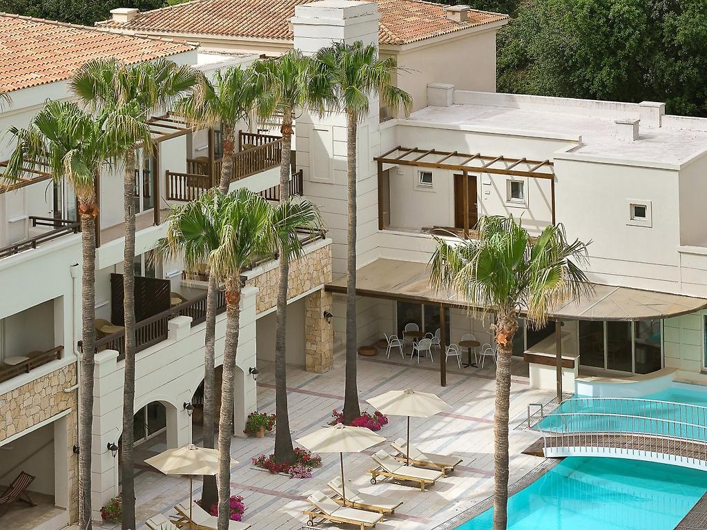 Grecotel Casa Adele, Moderne Hotelarchitektur mit stilvollen Balkonen und harmonischer Außenbeleuchtung.