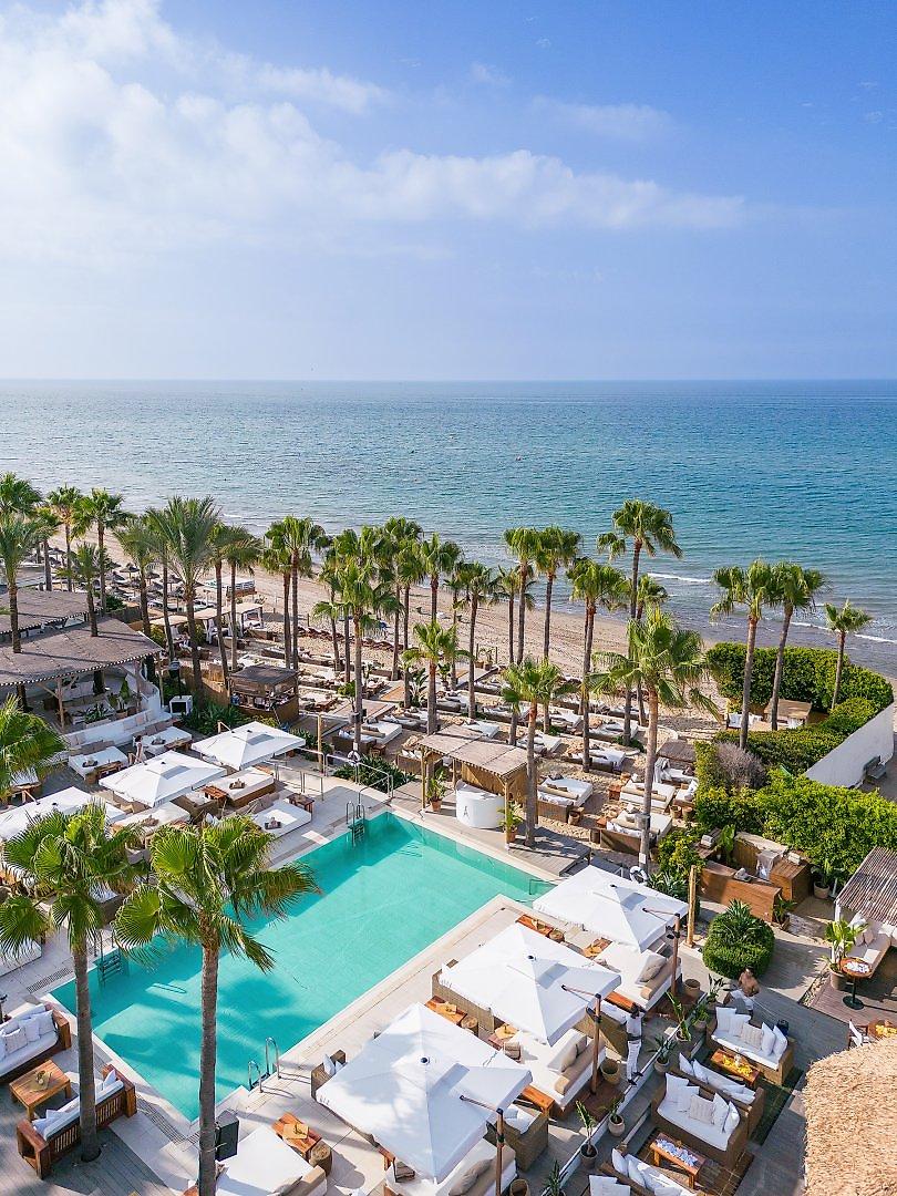 Hotel Don Carlos Marbella, Luxuriöser „Nikki Beach“ Club mit weißen Liegen, Sonnenschirmen und Poollandschaft.