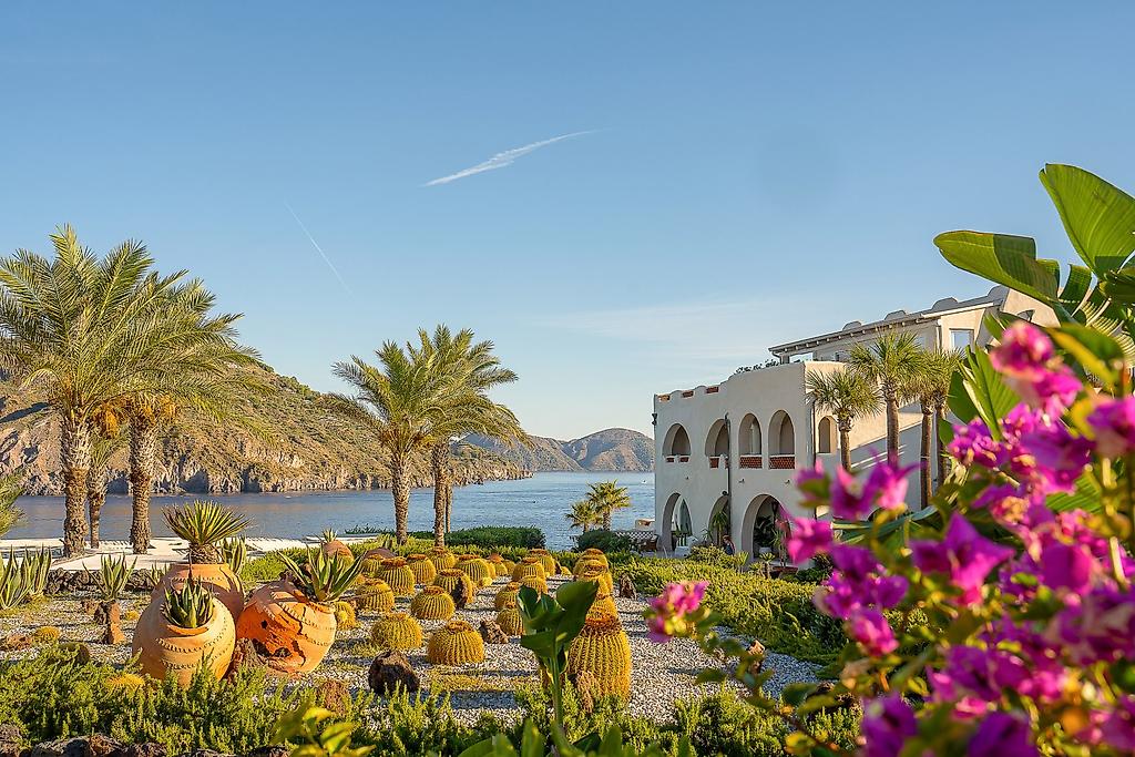 Therasia Resort Sea & Spa, Gepflegte, mediterrane Gartenanlage des Hotels mit Palmen, Sträuchern und grünen Rasenflächen.