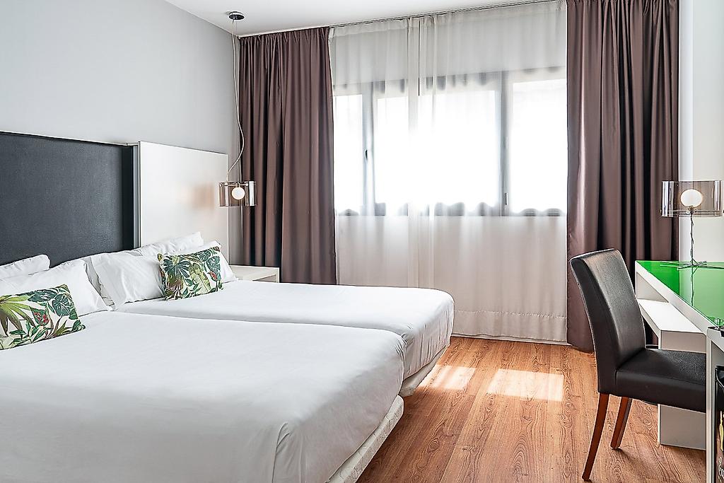Hotel Catalonia Málaga, Hell eingerichtetes Doppelzimmer mit Doppelbett, Sitzgelegenheit und moderner Dekoration.