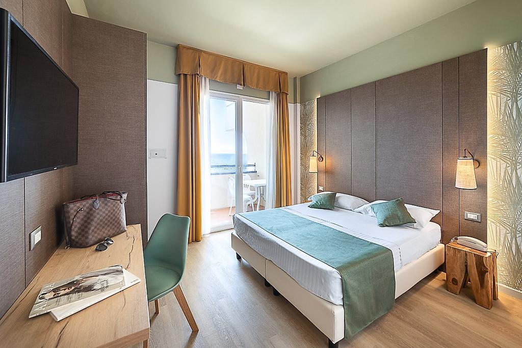 Hotel Life, Wohnbeispiel eines Hotelzimmers mit komfortablem Doppelbett, Kleiderschrank und Schreibtisch.
