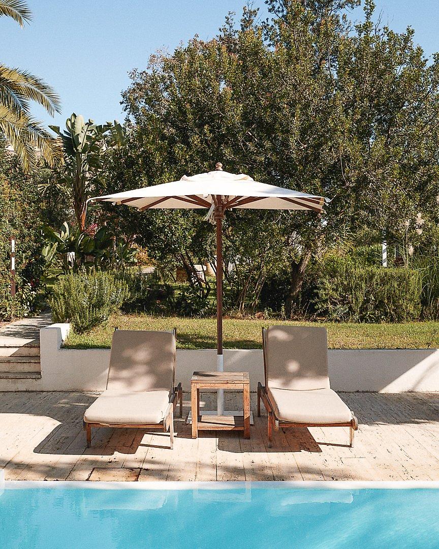Lanthia Resort, Sonnenliegen mit blauen Auflagen am Rand des hoteleigenen Swimmingpools.