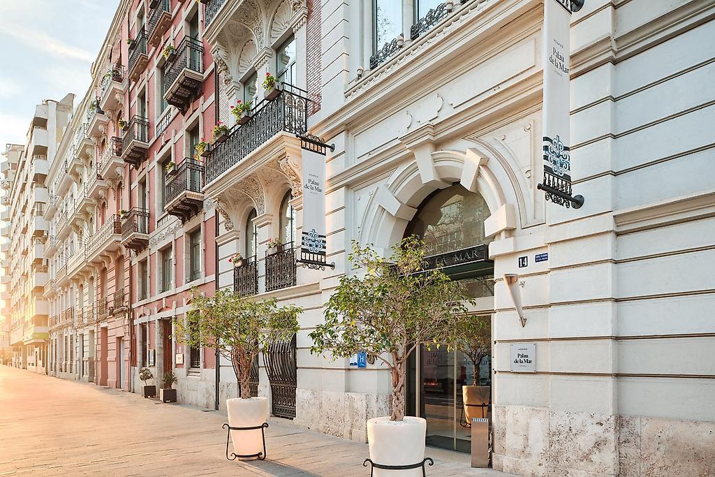 Hospes Palau de la Mar, Einladender Eingangsbereich des Hotelgebäudes in Valencia mit stilvoller Architektur und Bepflanzung.