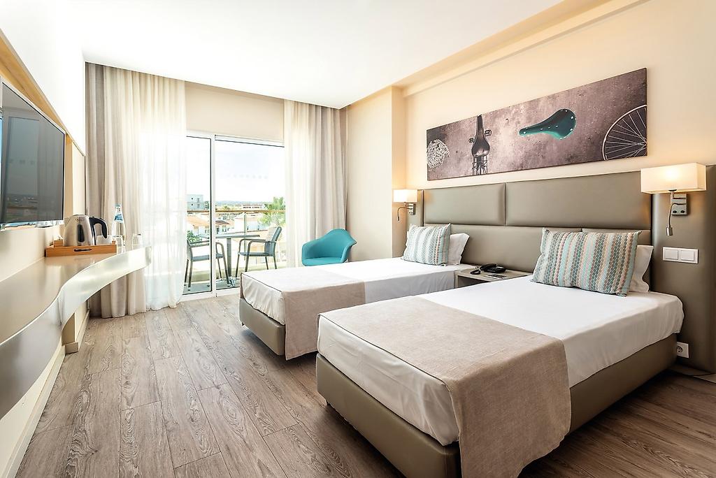 AP Maria Nova Lounge Hotel, Hell und modern eingerichtetes Hotelzimmer mit einem Doppelbett, hochwertigen Holzmöbeln und Zugang zum Balkon.