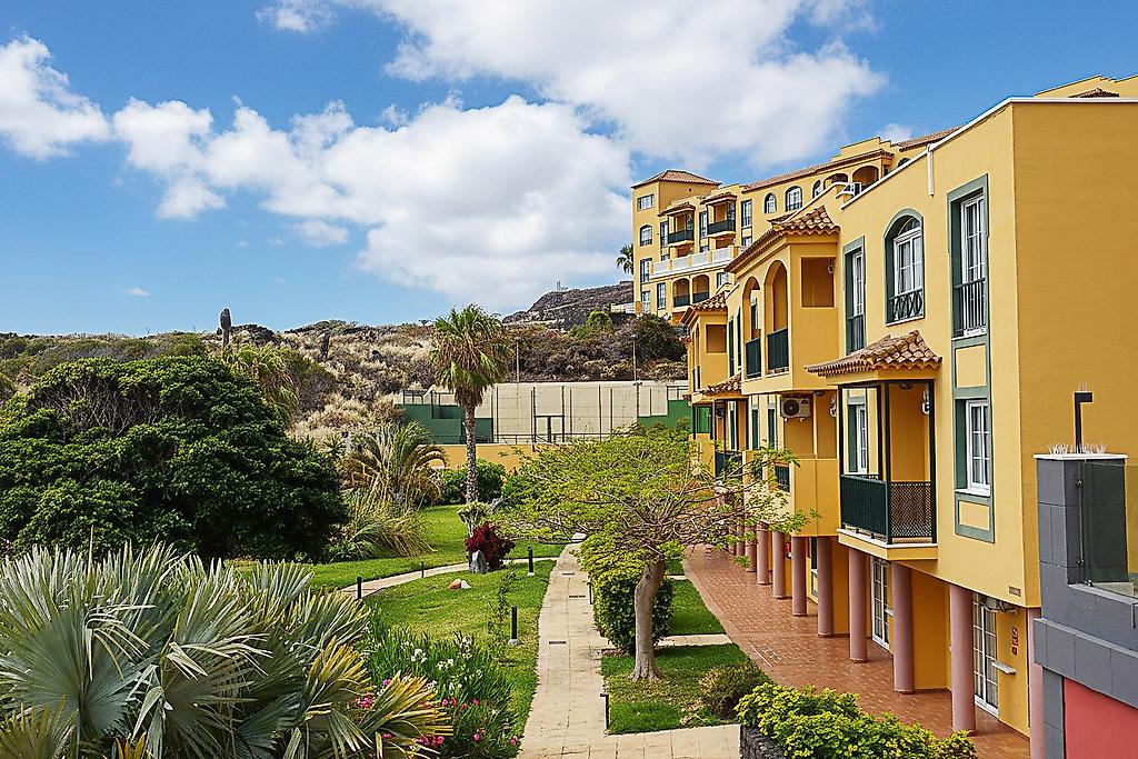 Hotel Las Olas, Gepflegter, grüner Hotelgarten in Spanien mit schattenspendenden Palmen, einer Rasenfläche und blühenden Sträuchern.