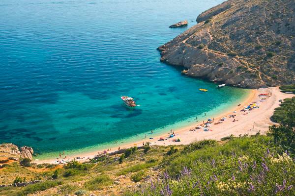 Badebucht mit Strand umgeben von Felsen und Wiese mit türkisblauem klaren Meer auf Krk