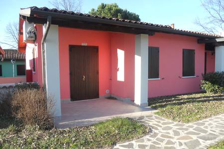The Garda Village, Eingangsbereich eines hellen Bungalows mit kleiner Terrasse und Bepflanzung.