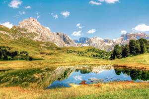 Grüne Wiesen mit kleinem Bergsee und den Dolomiten im Hintergrund in Südtirol