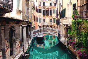 schmaler Kanal in Venedig mit kleiner Brücke und lila Blumen an den Fenstern
