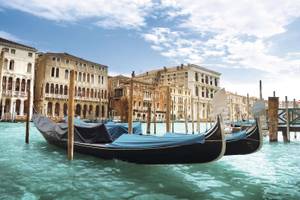 Zwei schwarze Gondeln auf türkisblauem Wasser mit Häusern im Hintergrund Venedig