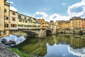 Brücke Ponte Veccio über dem Arno und gelbe Häuser am Ufer in Florenz bei Sonnenschein