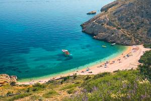 Badebucht mit Strand umgeben von Felsen und Wiese mit türkisblauem klaren Meer auf Krk