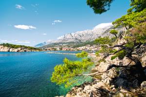 Küste Makarska mit Felsen und Bäumen und Bergen im Hintergrund