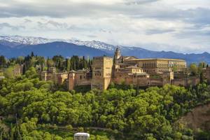Alhambra umgeben von Bäumen und Berge im Hintergrund in Granada
