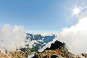 Bergkulisse mit Wolken die über dem Tal hängen und Sonnenschein
